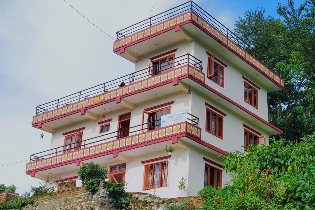 biały budynek z czerwonymi oknami i balkonem w obiekcie Patlekhet Eco Farmhouse w mieście Dhulikhel