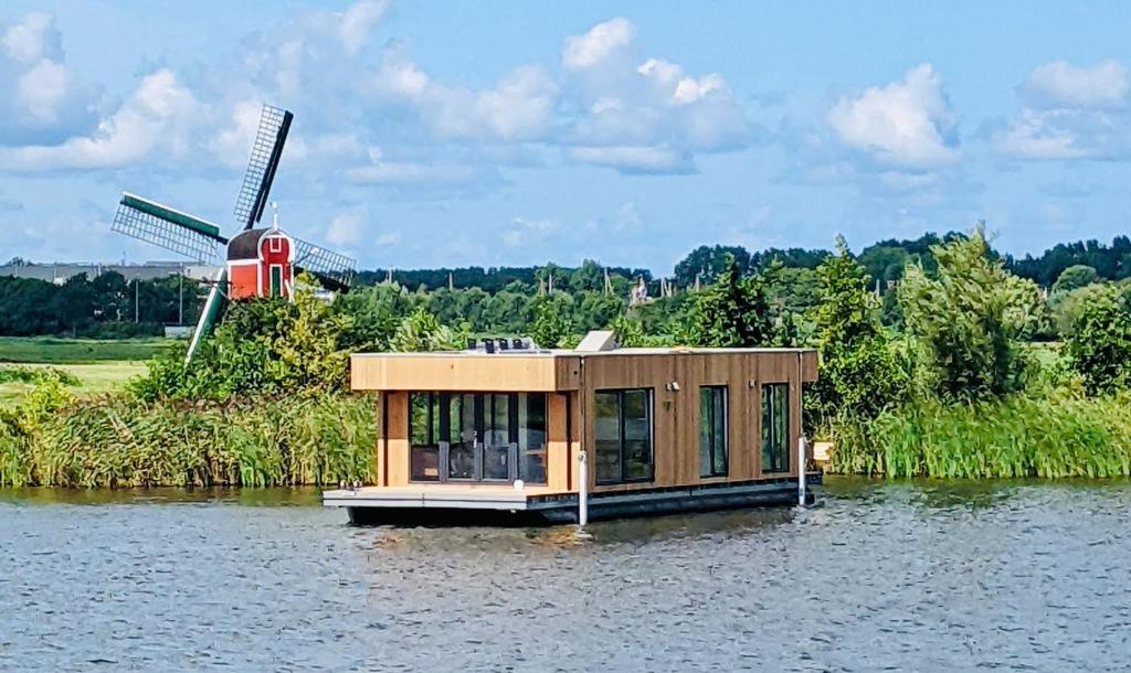 una pequeña casa en el agua con un molino de viento en Surla houseboat "Aqua Zen" Kagerplassen with tender, en Kaag