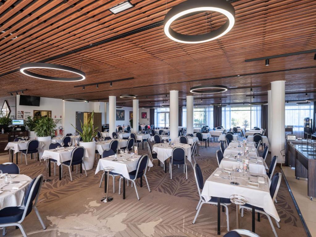 a restaurant with white tables and chairs and wooden ceilings at Westotel Le Pouliguen in Le Pouliguen