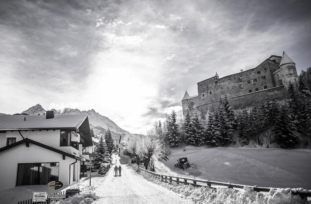 ein Schwarz-Weiß-Foto eines Schlosses und Leute, die eine Straße entlang gehen in der Unterkunft Alberts Bellevue Appartements in Nauders