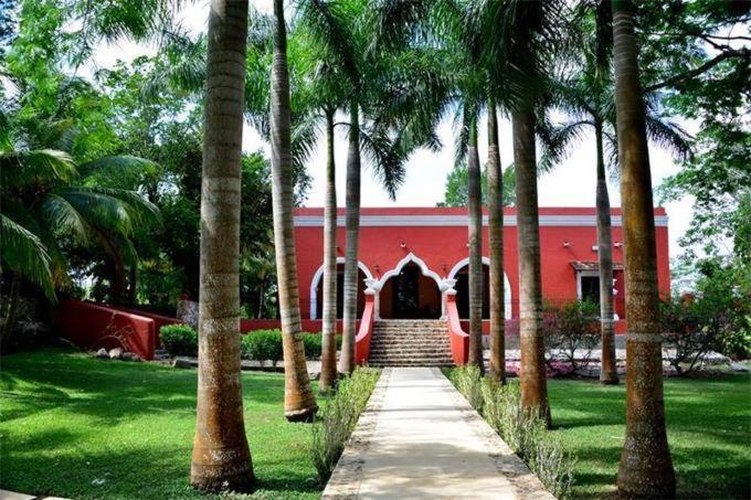 a red building with palm trees in front of it at Hacienda San Jose Poniente in Hoctún