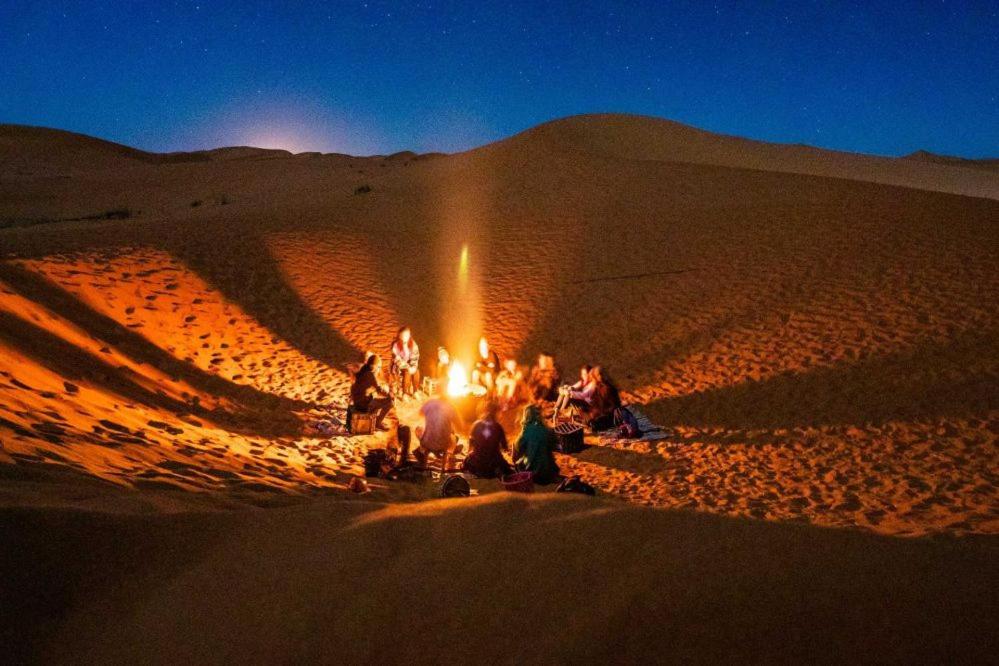 a group of people sitting around a fire in the desert at alsaif camp in Bidiyah