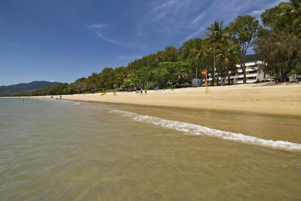 a beach with trees and a sandy shore with the ocean at On Palm Cove Beachfront Apartments in Palm Cove