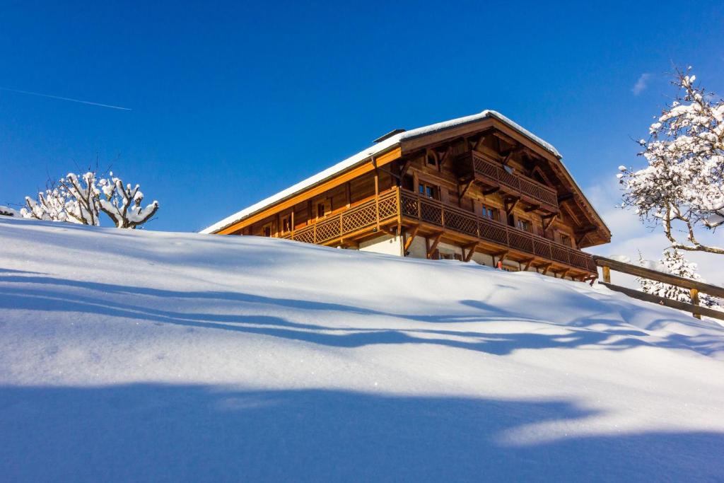 a building on a snowy hill with a shadow in the snow at Hôtel Restaurant La Ferme de Cupelin in Saint-Gervais-les-Bains