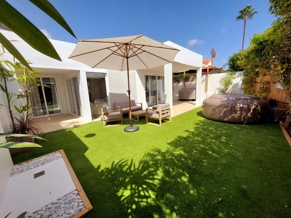 a patio with an umbrella and chairs and a lawn at Bungalow de diseño hidromasajes terraza y piscina. in San Bartolomé de Tirajana