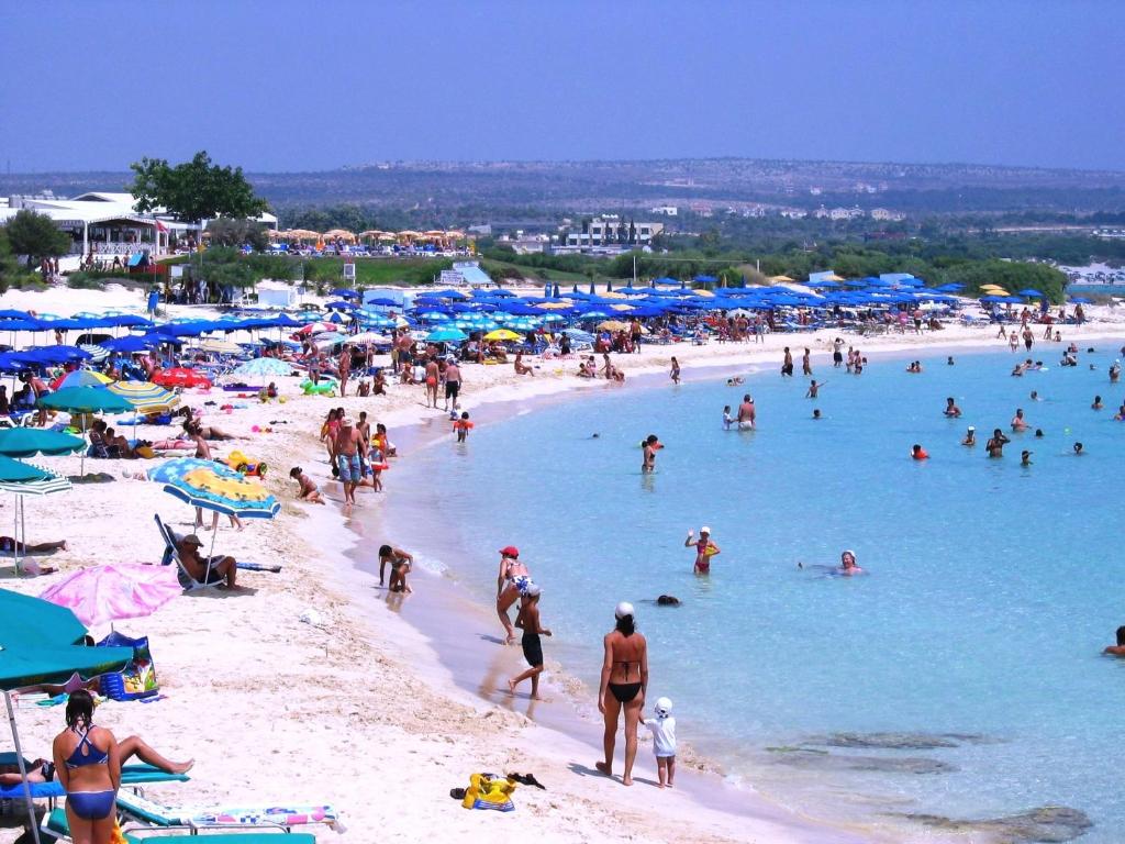 a crowd of people on a beach with blue umbrellas at Loutsiana Deluxe Apts in Ayia Napa