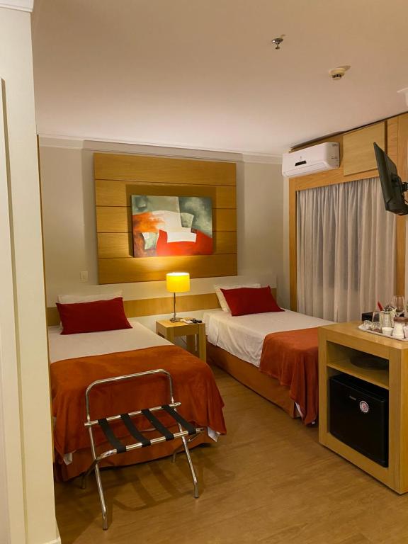 a hotel room with two beds and a desk at Suíte Aeroporto Congonhas in Sao Paulo