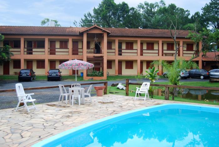 a hotel with a pool and chairs and an umbrella at Pousada Circuito das Aguas in Jaguariúna