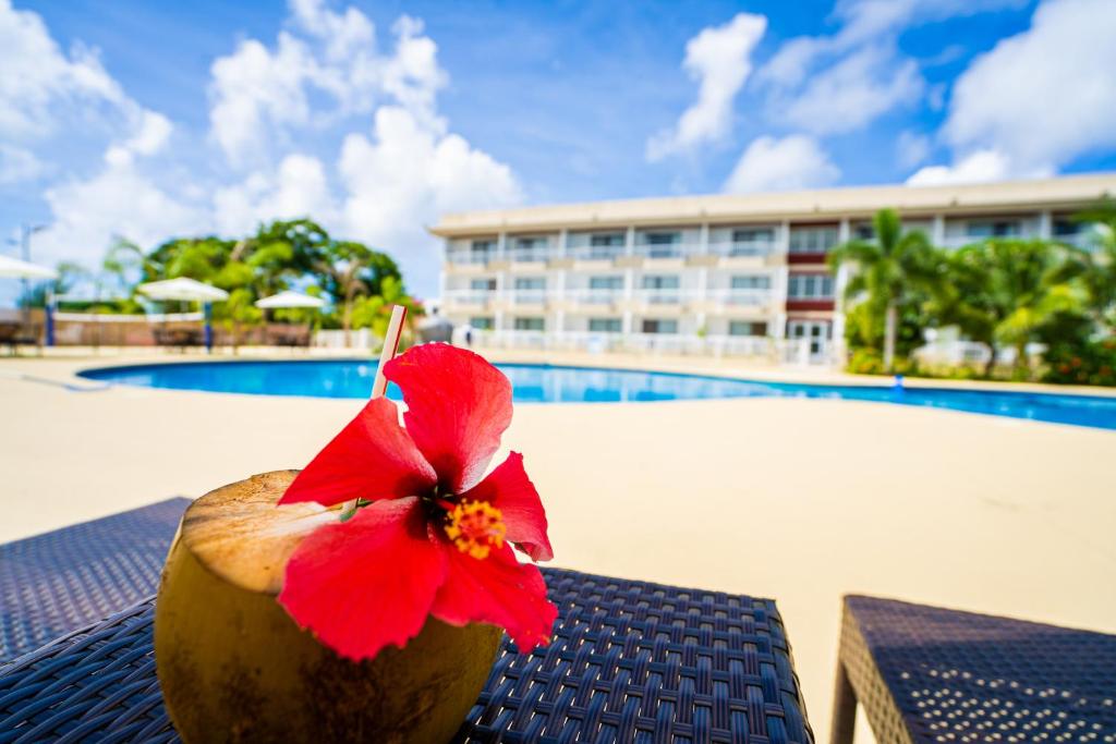 een kokosnoot met een rode bloem op een tafel naast een zwembad bij Paradiso Resort & Spa in Saipan