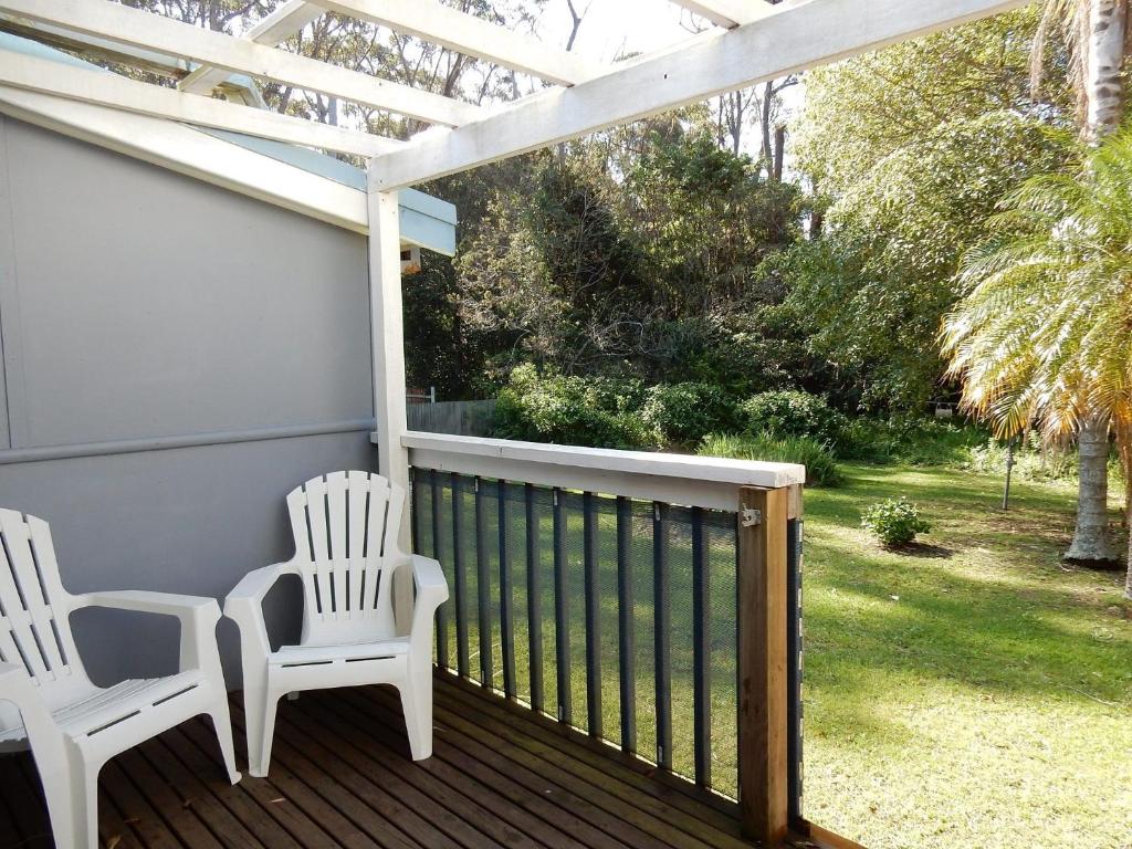 two white chairs sitting on a porch with a pergola at Donlan's Beach Cottage in Mollymook