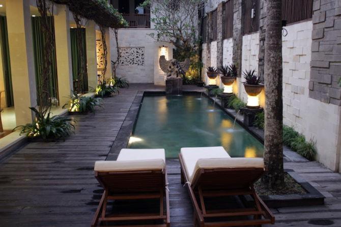 a swimming pool in a courtyard with two lounge chairs at Cinta inn in Ubud
