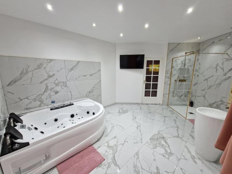un bagno bianco con vasca e lavandino di Maison Chic avec jacuzzi. UrbanSpa60 a Nogent-sur-Oise