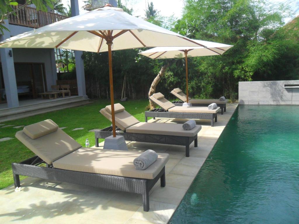 four lounge chairs and an umbrella next to a swimming pool at Ju'Blu Hotel in Lovina