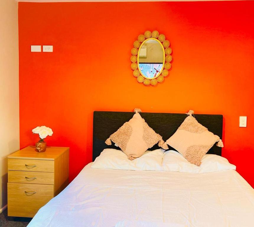 1 dormitorio con pared de color naranja, cama y espejo en Private studio Auckland Self Checkin and 2 Parking Netflix Prime, en Auckland