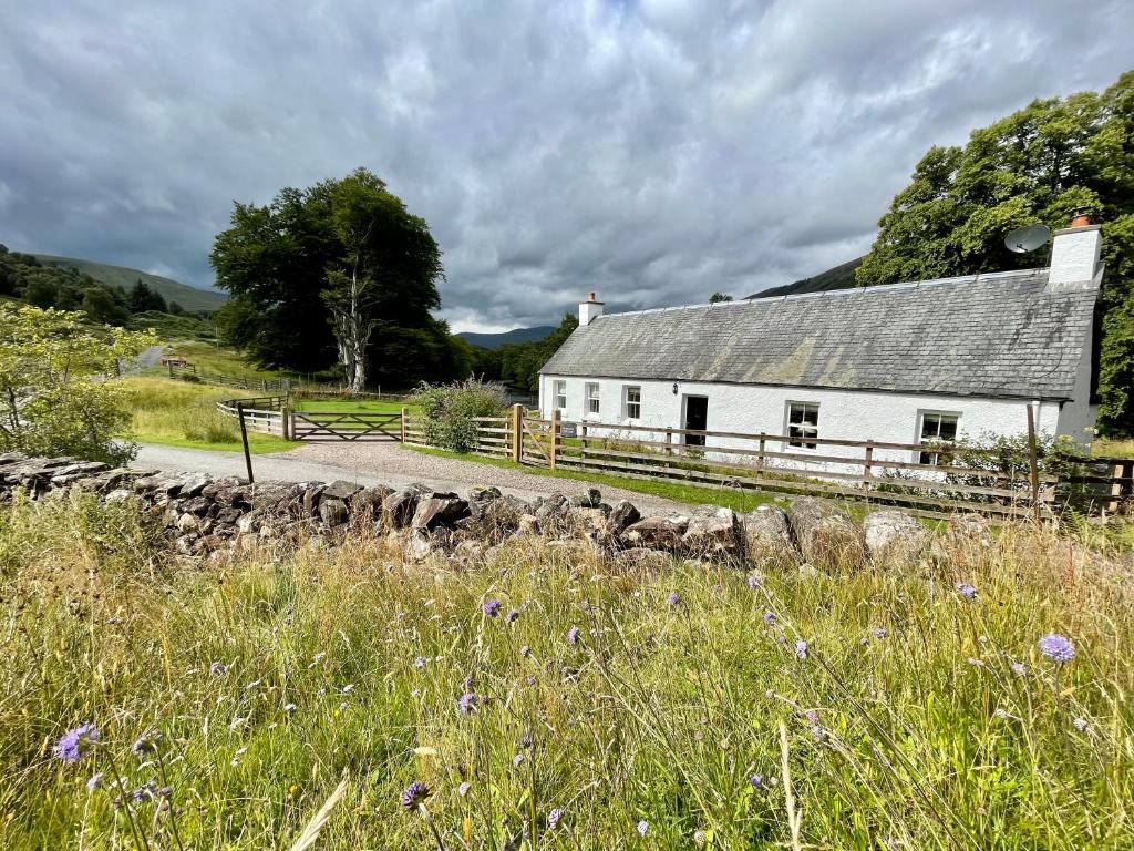 a white house with a fence and a field at Riverside Cottage, Bridge of Balgie, Glenlyon, Perthshire 