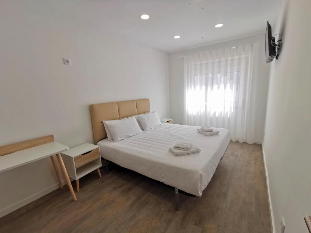 a white bedroom with a bed and a window at Vila Alexandra in Costa da Caparica