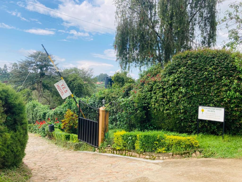 a garden with a gate and bushes and a sign at Yes Hostel in Fort Portal