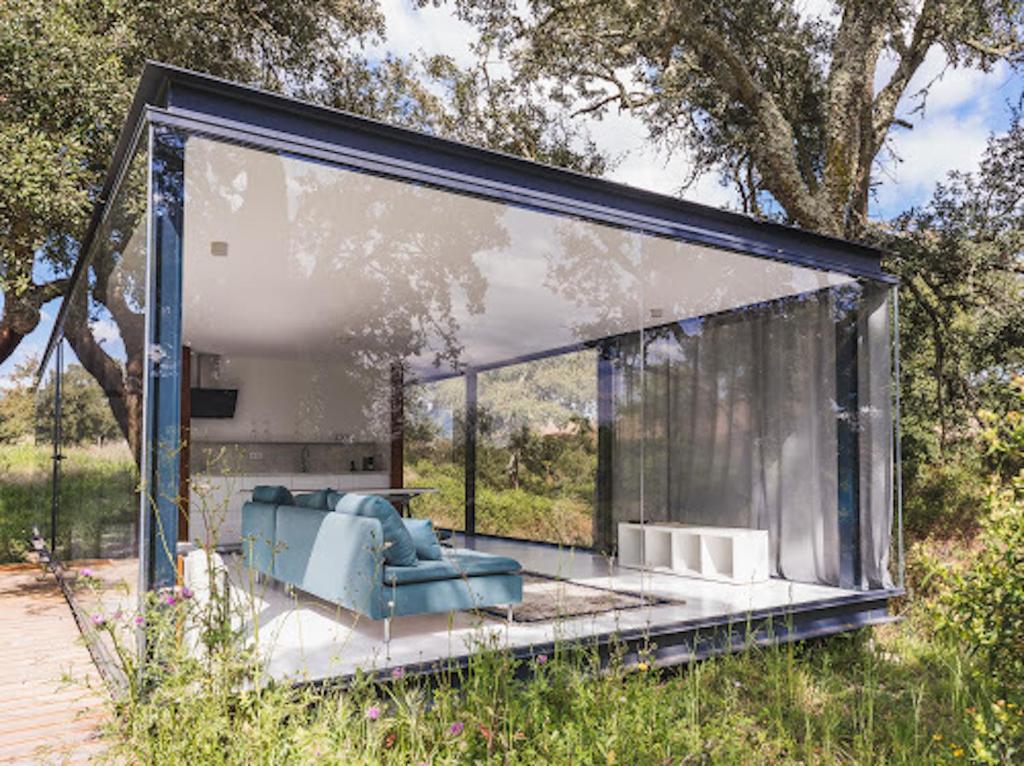 Una casa de cristal con un sofá azul. en One bedroom property with lake view shared pool and enclosed garden at Montemor o Novoa, en Montemor-o-Novo