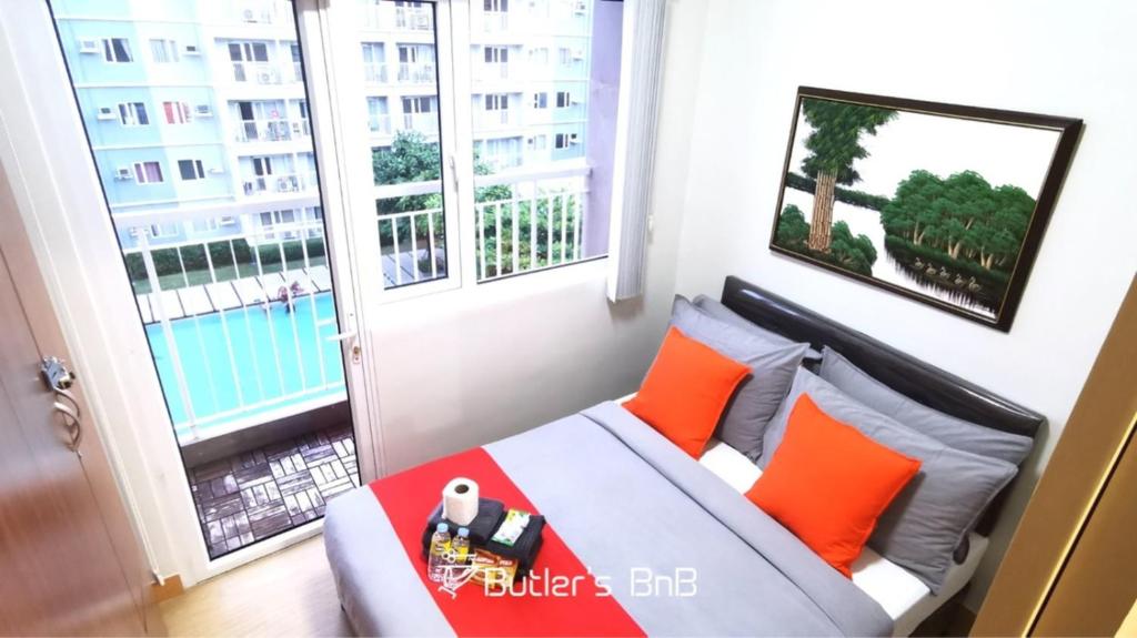 een slaapkamer met een bed met oranje kussens en een raam bij Butler's BnB @ Trees Residences QC Phil in Manilla