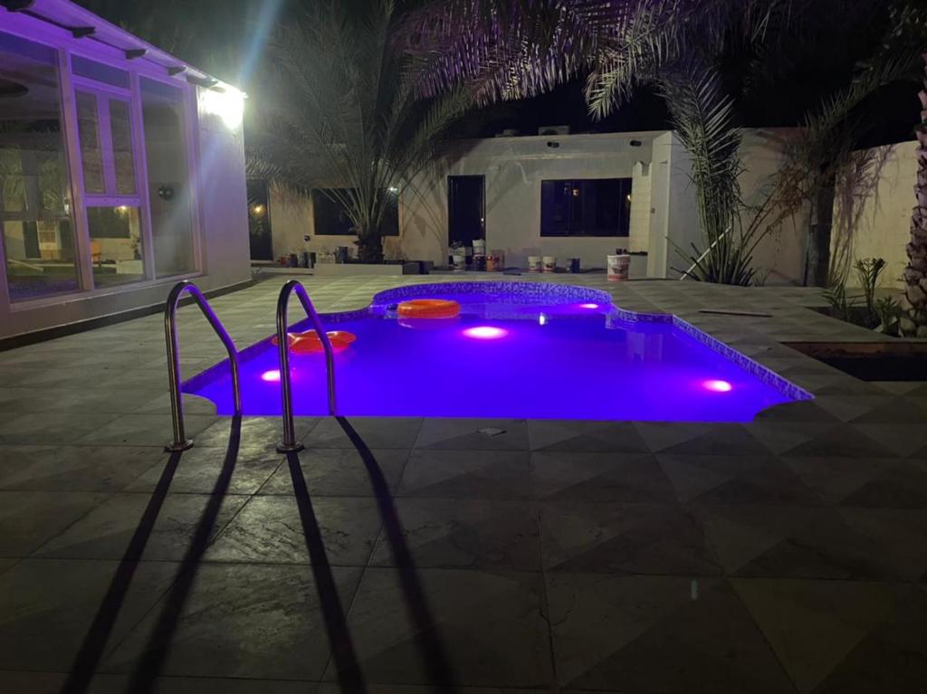 uma piscina com luzes roxas num quintal à noite em Dar Alhamra INN نزل دار الحمراء em Al Hamra
