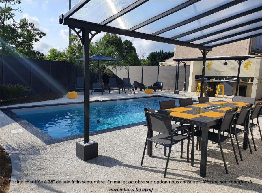 a dining table and chairs under a pergola next to a pool at Villa des palmiers - Magnifique villa avec piscine privée et chauffée selon saison in Bon-Encontre