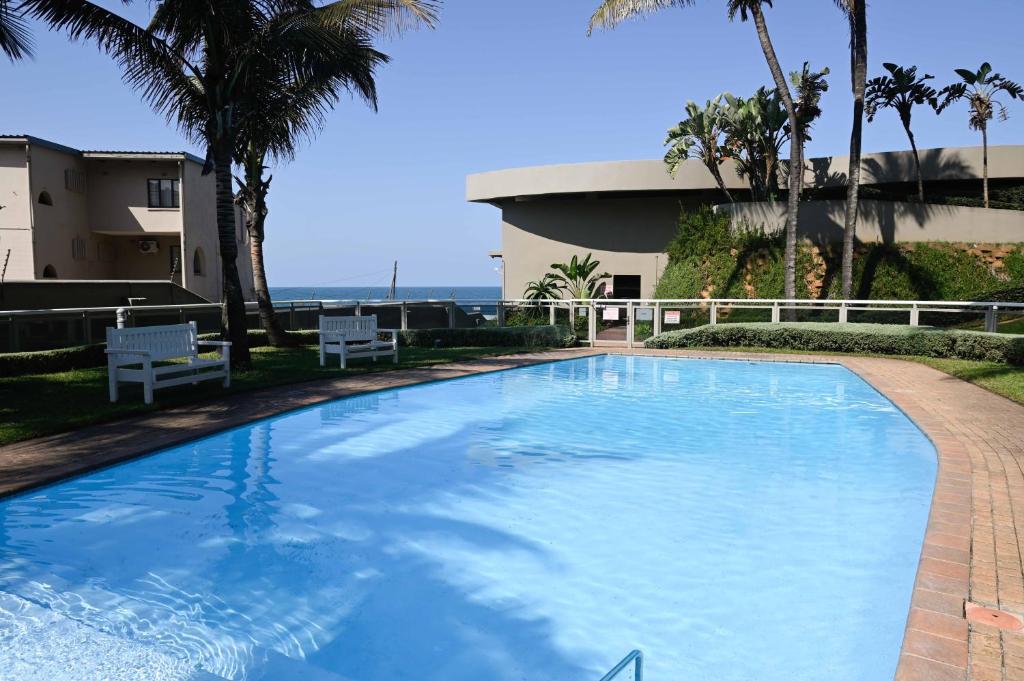 a large swimming pool with palm trees and a building at Surfside Ballito - Family Only in Ballito