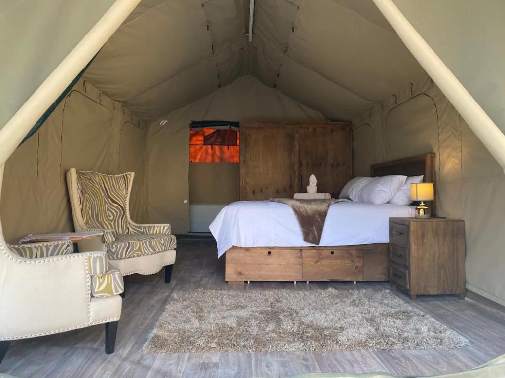 1 dormitorio en una tienda de campaña con 1 cama y sillas en Vlakkieskraal Farmstay - Nyala Tented Camp, en Bela-Bela