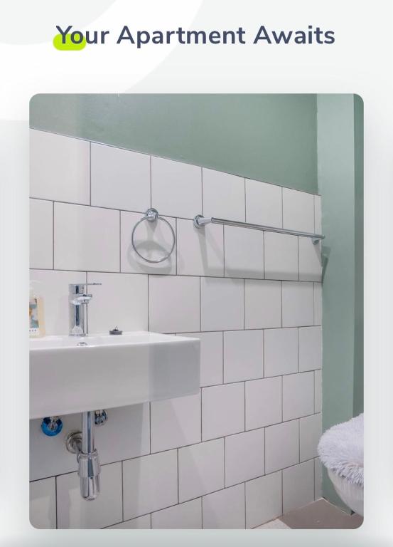 uma casa de banho em azulejos brancos com um lavatório e um espelho. em Batchelor City Studio Apartment em Durban