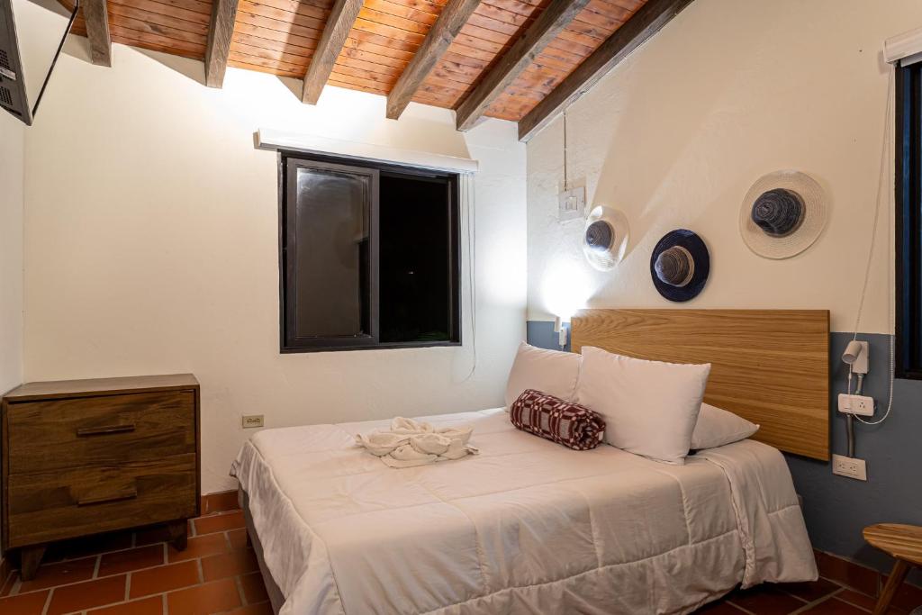 a bedroom with a bed with white sheets and a window at Soy Local Guatape in Guatapé