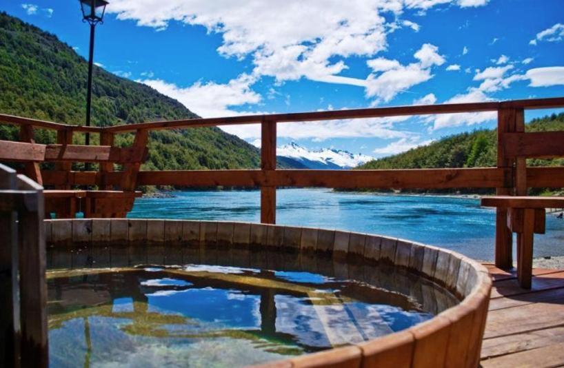 a hot tub with a view of a river and mountains at Green Baker Lodge in Puerto Bertrand