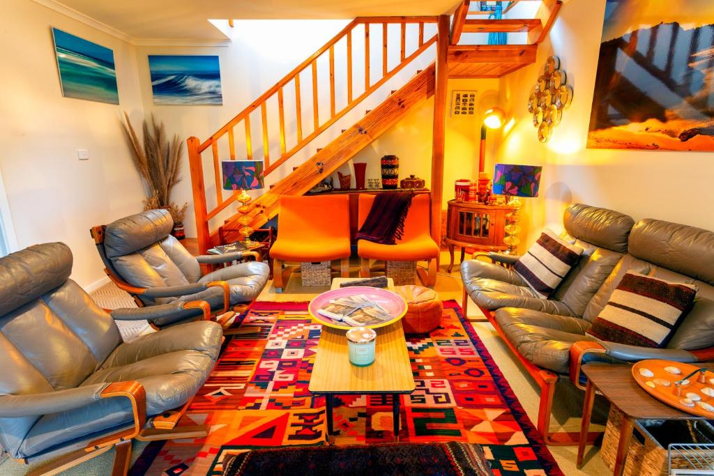 a living room with leather furniture and a staircase at Retro Dunes Venus Bay - WiFi, Netflix, BBQ, linens, pets OK in Venus Bay