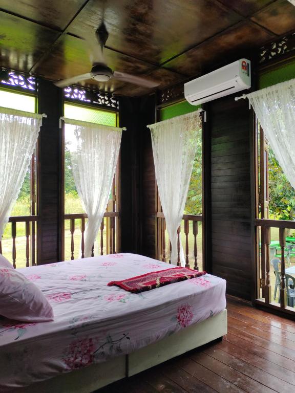 a bedroom with a bed with white curtains and windows at Homestay Kampung Den in Kampong Jimah