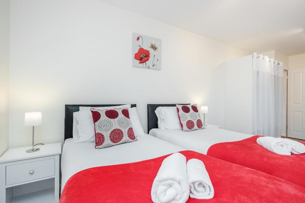 two beds with red and white pillows in a bedroom at MPL Apartments - Queens Broadway F4 in Watford