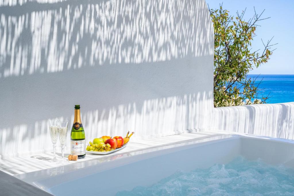 a bottle of wine and a bowl of fruit next to a bath tub at Poseidon Blue Gastronomy Hotel in Afiartis