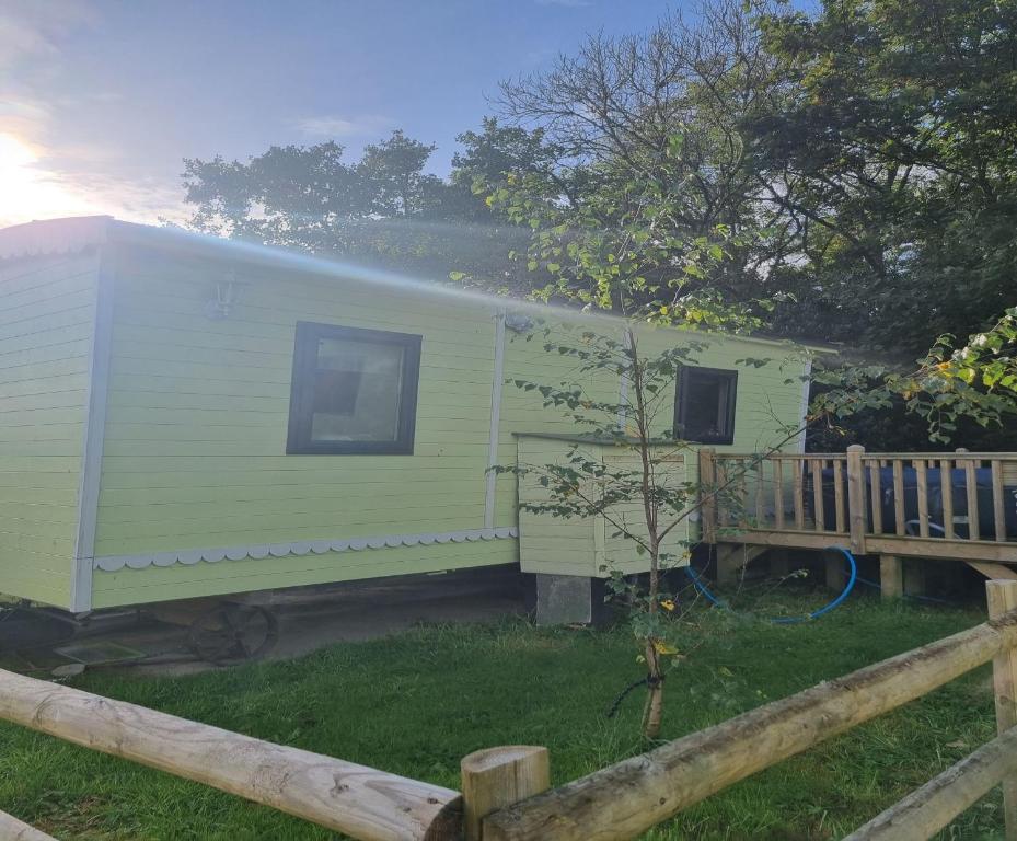 a green trailer parked next to a wooden fence at Glamping Hut - Sleeps 2 hot tub & parking in Garthbeibio