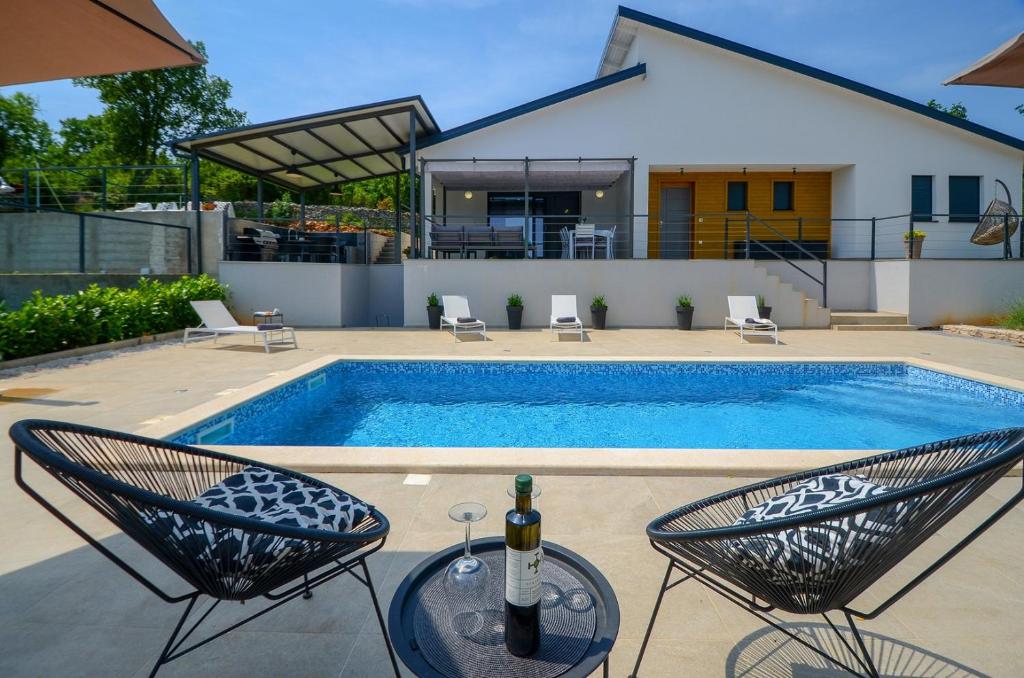 una piscina con due sedie e un tavolo con una bottiglia di vino di Villa Bellavu a Rakalj