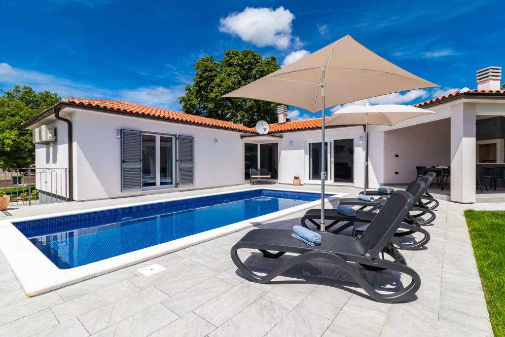 a villa with a swimming pool and two lounge chairs and an umbrella at Villa NaNa in Orbanići