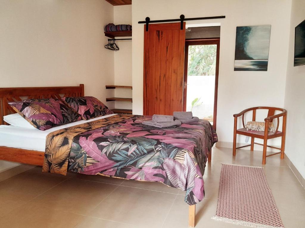 a bedroom with a bed and a chair and a window at Hakuna Studios Barra do Sahy in Barra do Sahy