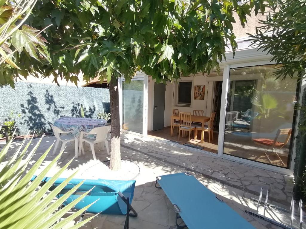 un patio con mesa y sillas bajo un árbol en LE SOLEIL D'OR en Sainte-Maxime