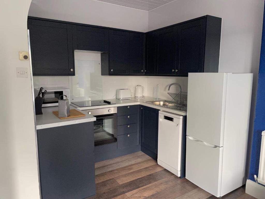 a kitchen with black cabinets and a white refrigerator at The Wee Lion in Troon