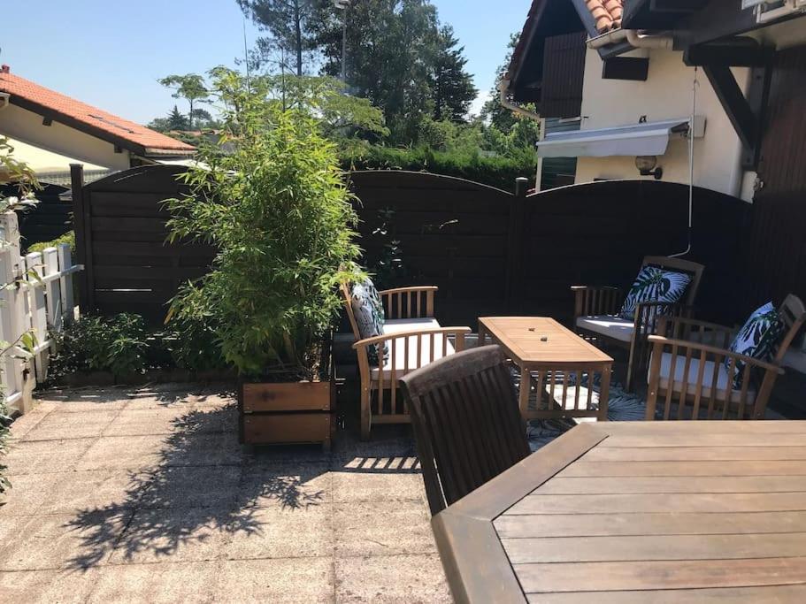 een patio met een houten tafel en stoelen en een hek bij Villa patio classée proche océan in Capbreton