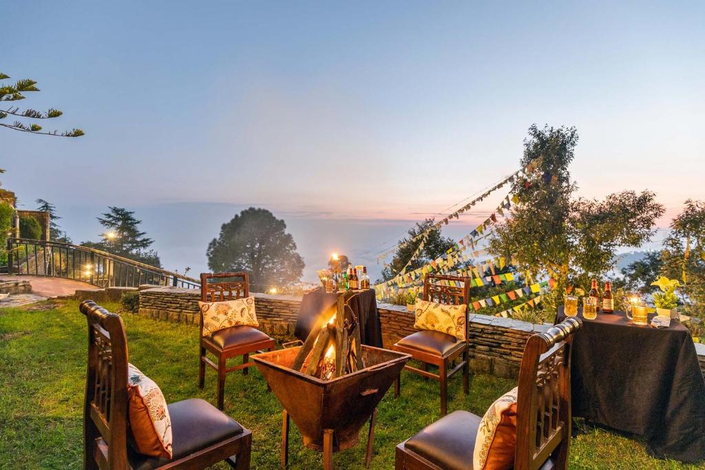 a group of chairs around a table with a fire at StayVista at Stonehill Manor with Outdoor Sitting in Dharamshala
