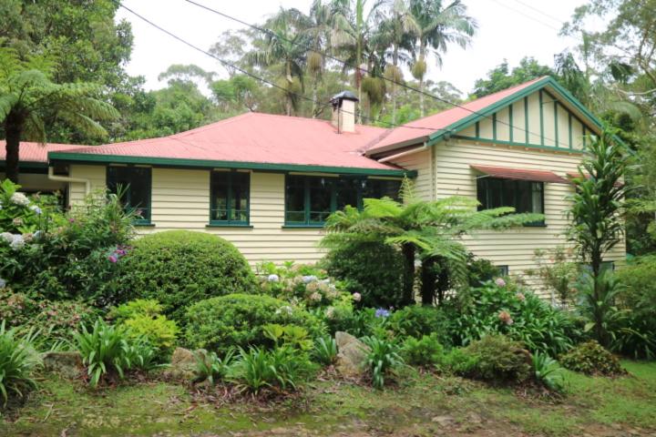 ein gelbes Haus mit rotem Dach und einigen Büschen in der Unterkunft Rosella's On Springbrook in Springbrook