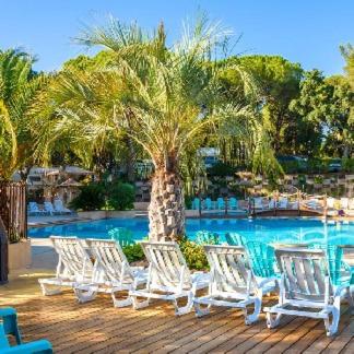 a group of white lounge chairs next to a palm tree at Mobile home 5-pers Camping Leï Suves-Côtes d&#39;Azur-including airco in Roquebrune-sur-Argens