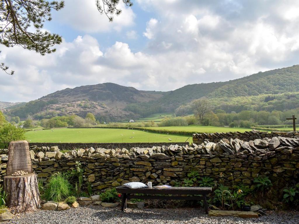 a bench in front of a stone wall with a field at Swingletree Cottage in High Nibthwaite