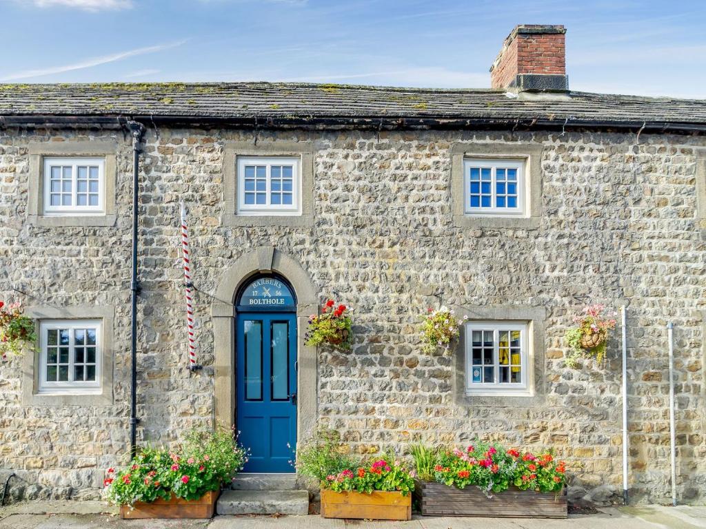 an old stone house with a blue door and flowers at Barbers Bolthole in Masham