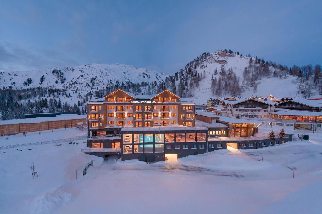 ein großes Gebäude im Schnee mit einem Berg in der Unterkunft Das Tauernherz in Obertauern