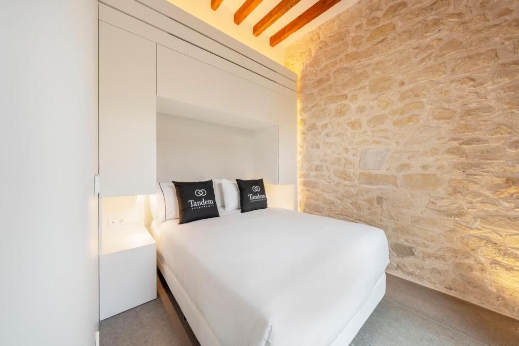 ein Schlafzimmer mit einem weißen Bett und einer Steinmauer in der Unterkunft Tandem Pórtico Alicante Suites in Alicante