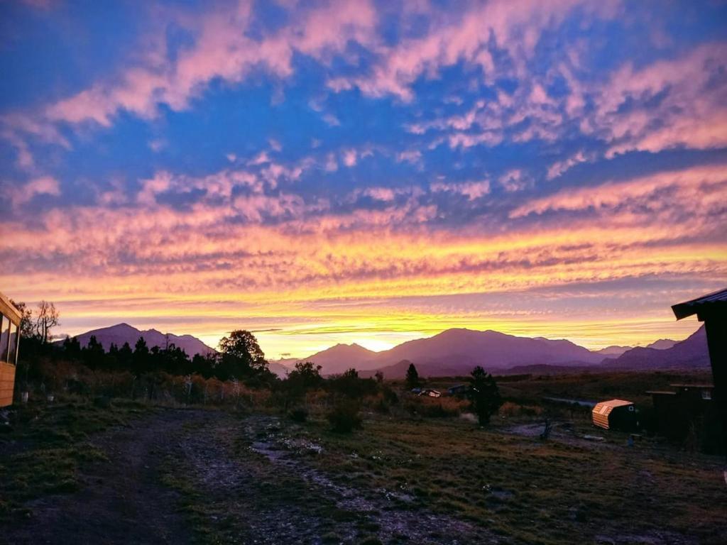 un coucher de soleil sur un champ avec des montagnes en arrière-plan dans l'établissement Cabañas Ladera de Nant y Fall -Tiny Houses-, à Trevelín