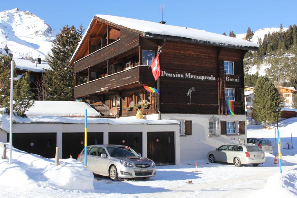 un edificio con auto parcheggiate fuori nella neve di Pension Mezzaprada a Arosa